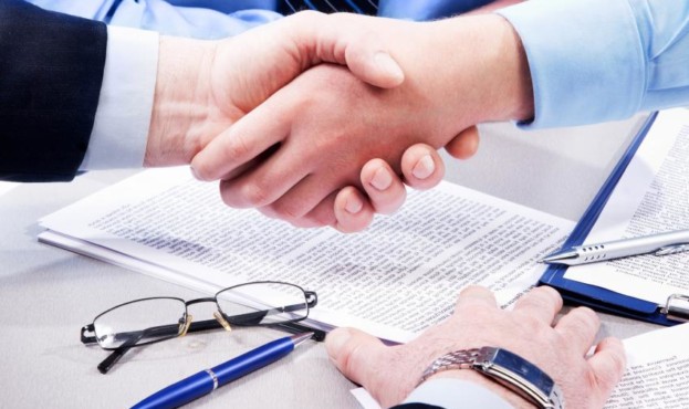 Close-up of business handshake over workplace with documents, pens, glasses