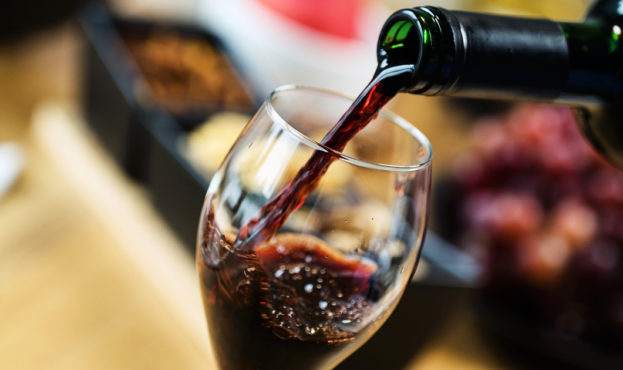 Red wine pouring into a wine glass at a tasting with various types of appetizers.