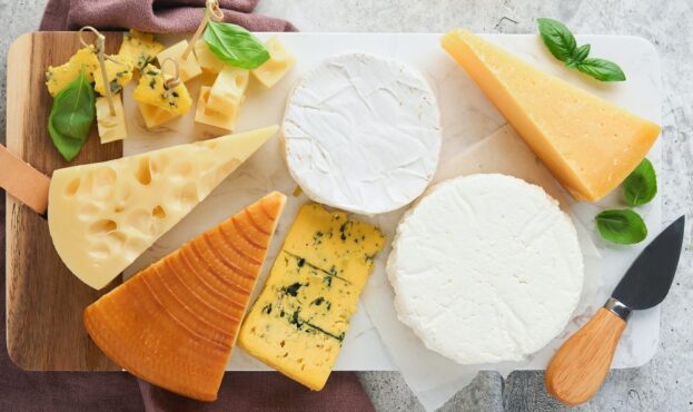 Set or assortment cheeses. Maasdam, smoked cheese, camembert, blue cheese, parmesan, brie cheese with basil and pepper on on white marble board white wooden old background. Top view. Free copy space.
