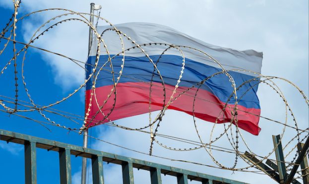 Russian flag behind barbed wire against cloudy sky