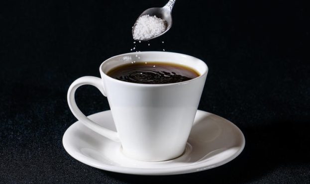 Sprinkling of sugar in a white cup of coffee